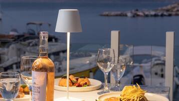 A table set for a meal with a bottle of wine, glasses, and plates of food, overlooking a marina with boats.
