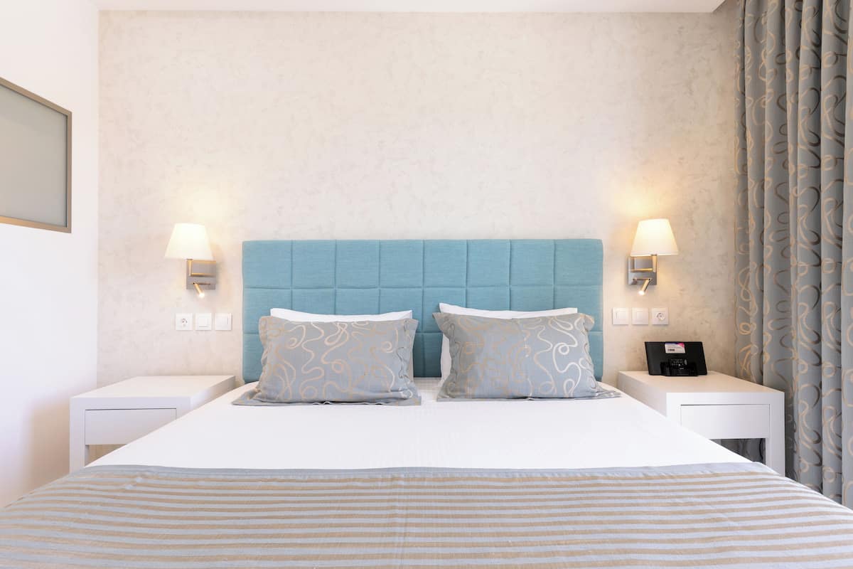 Hotellihuone, jossa on suuri sänky, kaksi yöpöytää, yölamppu ja sängynpääty.