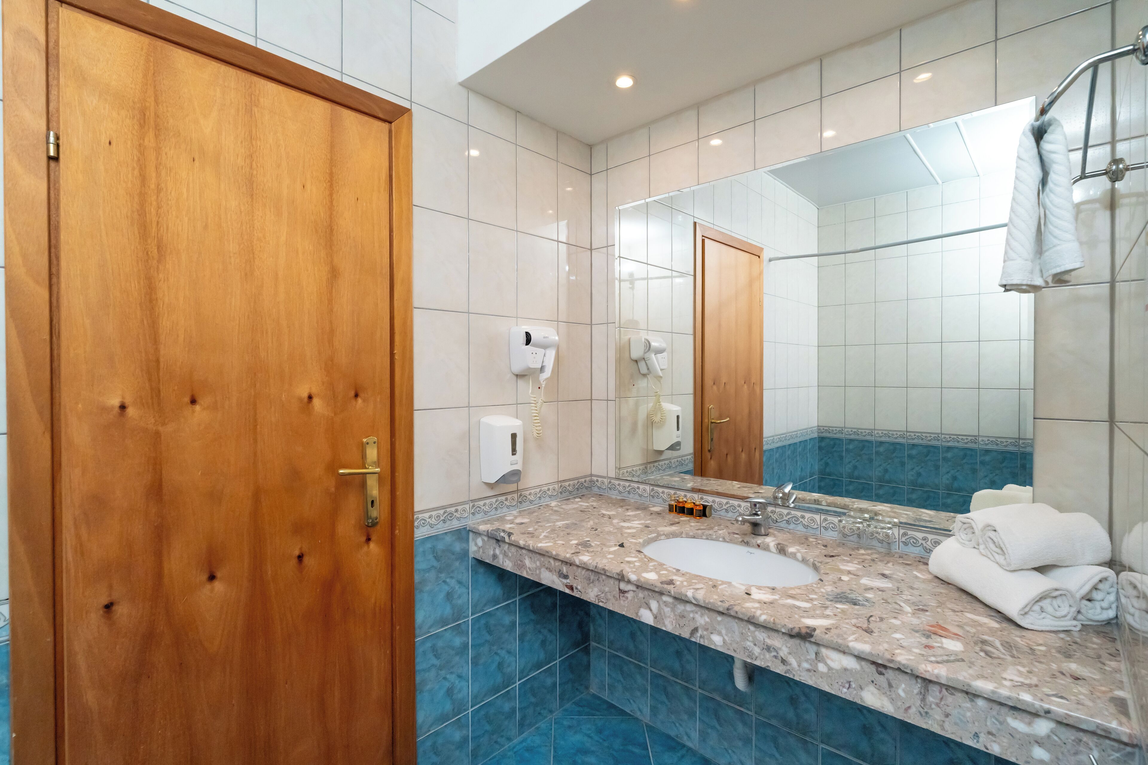 Une salle de bain avec une porte en bois, un lavabo en marbre, un grand miroir et un porte-serviettes.