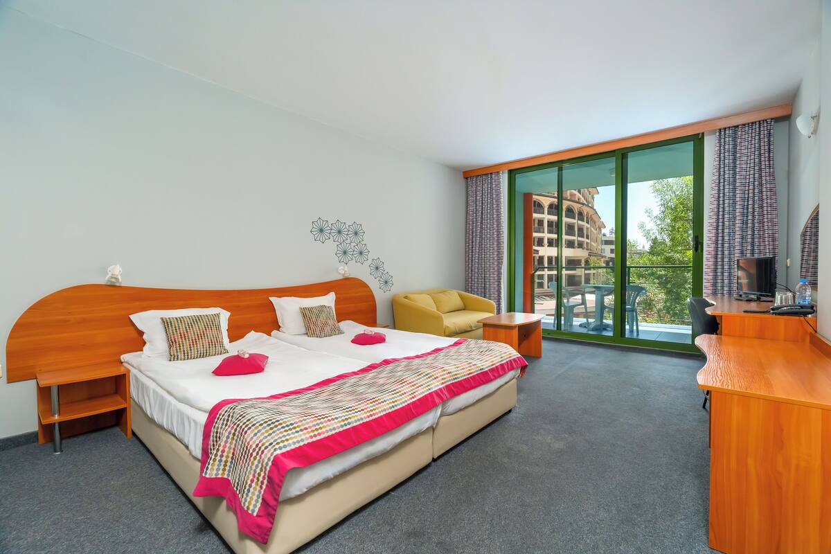 A hotel room with a large bed, a desk, a chair, and a view of the outside.