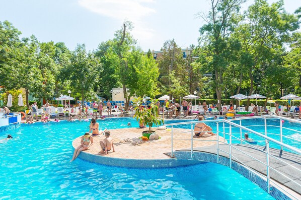 Una piscina con múltiples carriles, rodeada de árboles y sombrillas.