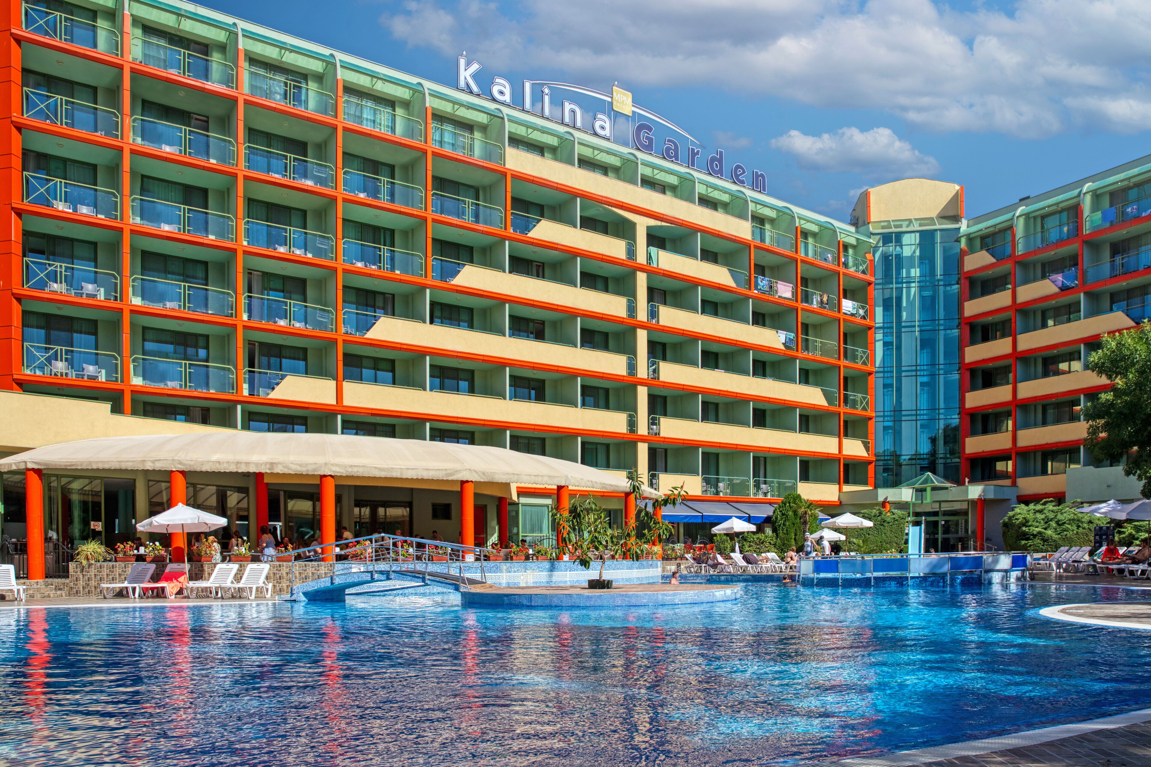 Een hotel met een zwembad, meerdere balkons en een overdekt terras met lounge stoelen.