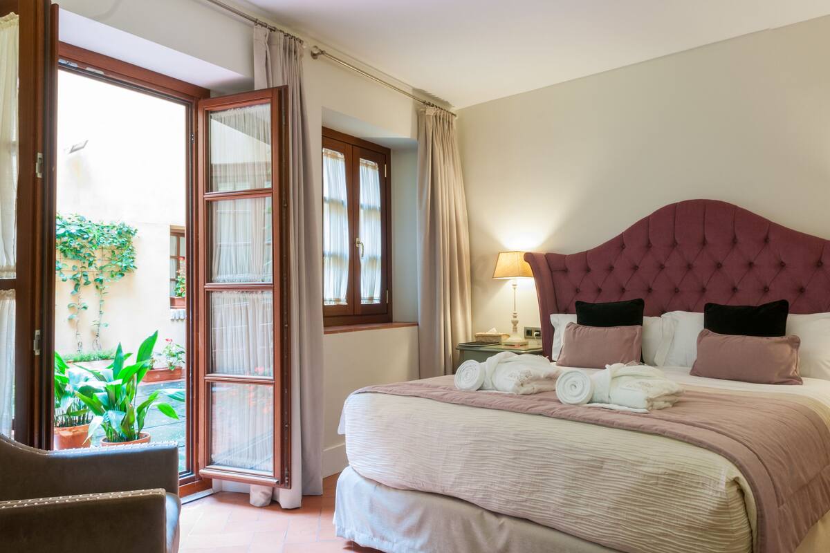 Ein Schlafzimmer mit einem großen Bett, zwei Nachttischen, einem Fenster mit Vorhängen und Blick nach draußen.
