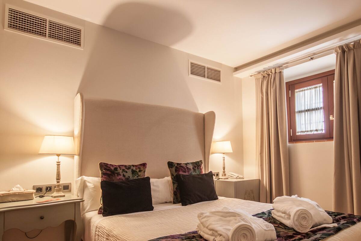 Ein Hotelzimmer mit einem großen Bett, zwei Nachttischlampen, einem Schreibtisch und einem Fenster mit Vorhängen.