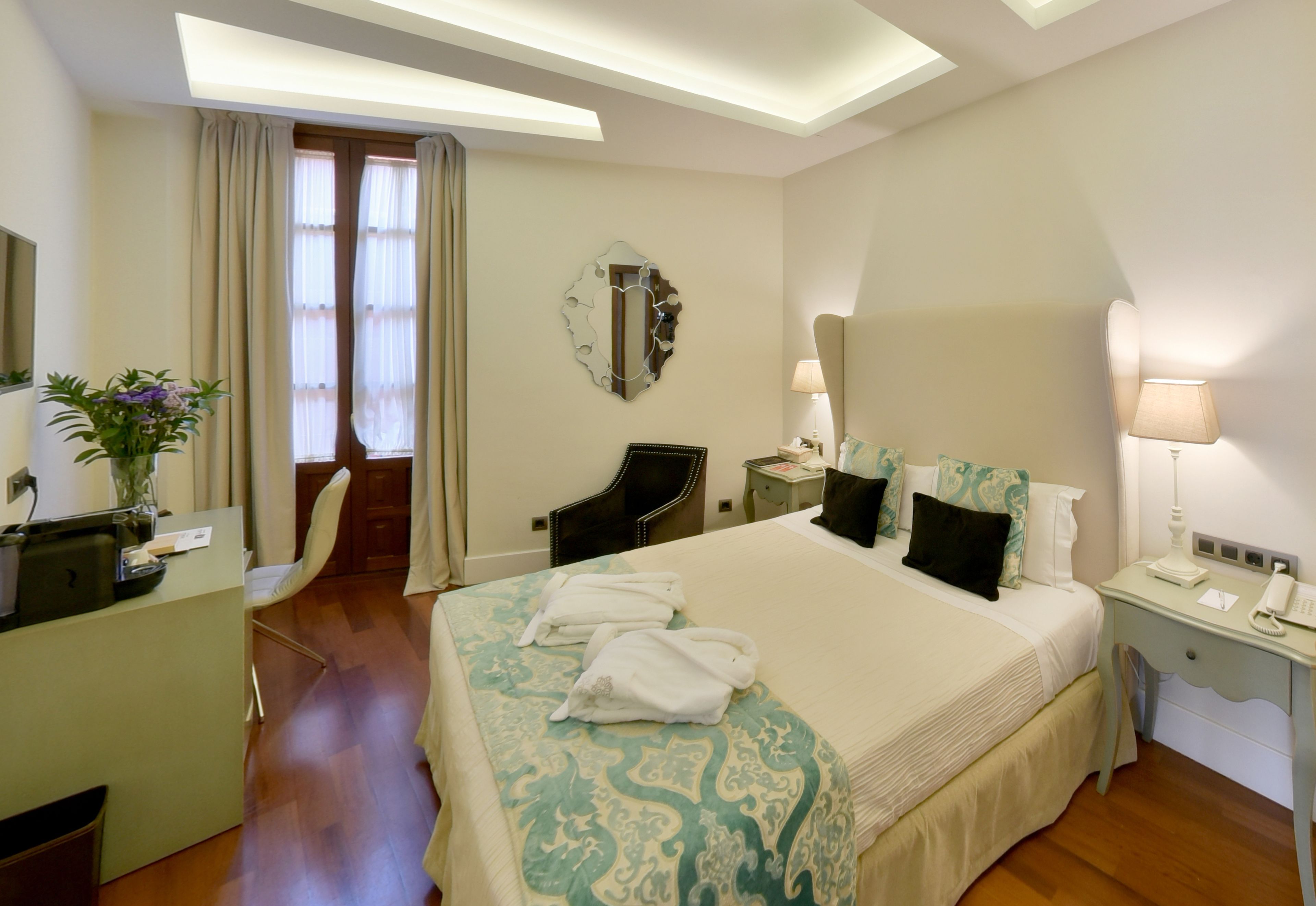 A hotel room with a large bed, a desk, a chair, a mirror, and a window with curtains.