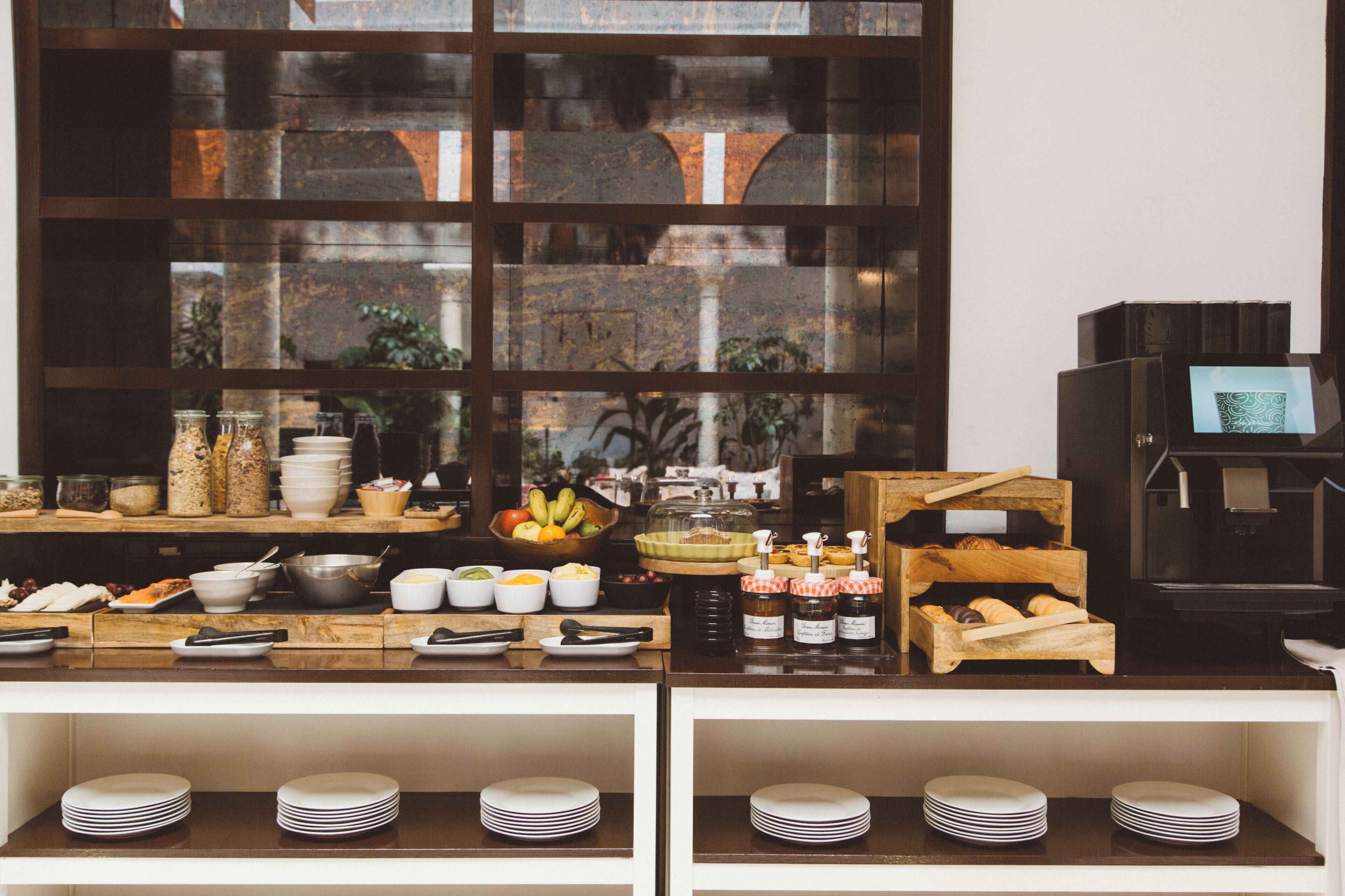 Una mesa de buffet con distintos alimentos y salsas, una máquina de café y vistas a través de una ventana.