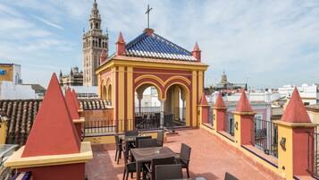 Terraza en la azotea con mobiliario exterior, un pequeño pabellón y vistas a una torre histórica.