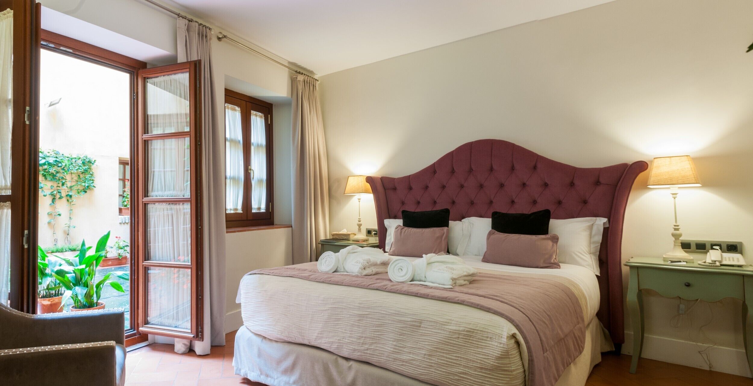 A bedroom with a large bed, two bedside tables, a window with curtains, and a view of the outside.