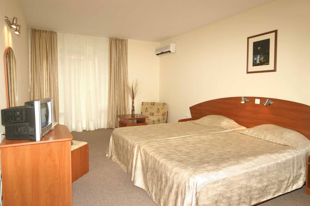 A hotel room with a wooden bed, a desk with a television, a nightstand, and a picture on the wall.