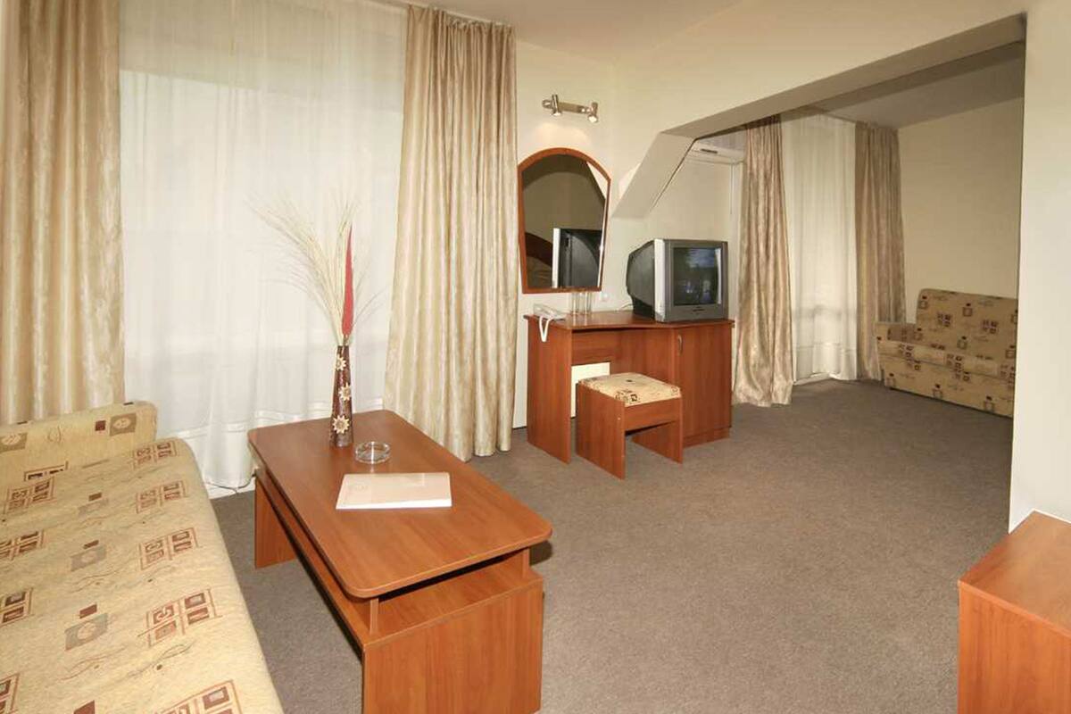 A hotel room with a wooden desk, a television, a mirror, and a patterned sofa.