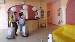 Zona de recepción con mostrador, un sofá amarillo y una mesa de recepción con un cartel.