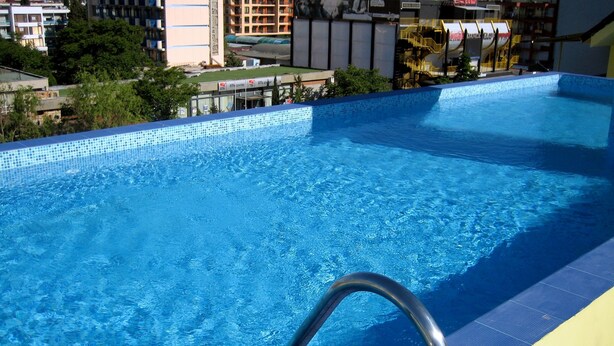 Una piscina con una escalera metálica, rodeada de edificios y árboles.
