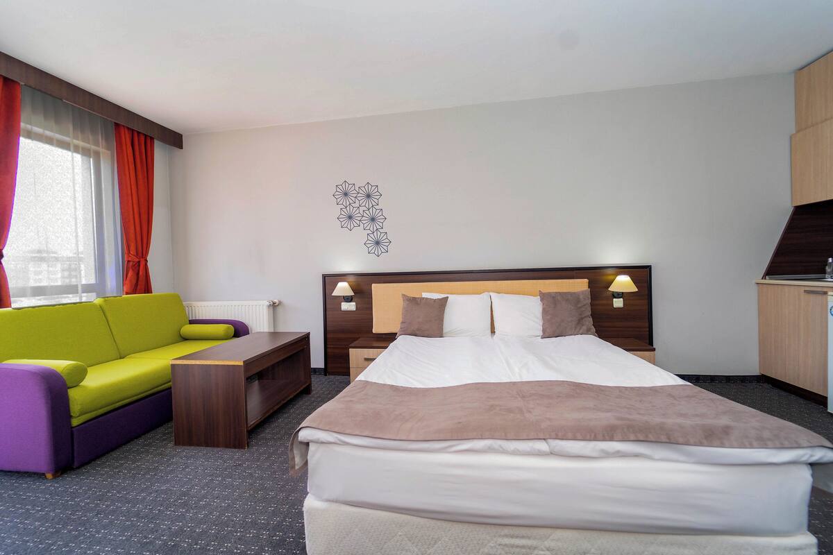 A hotel room with a bed, a sofa, a desk, and a wall decoration.