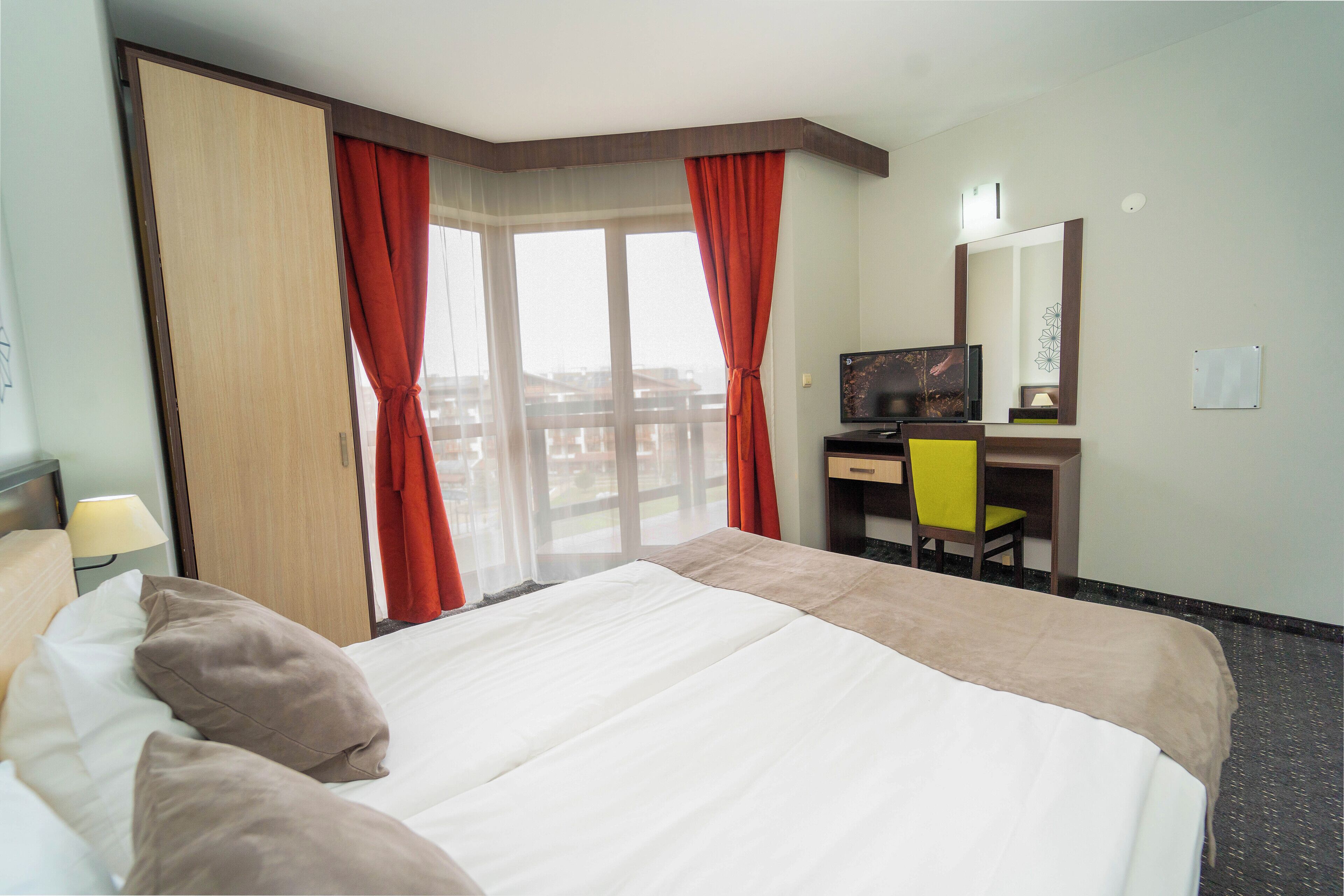 Une chambre d’hôtel équipée d’un lit, d’un bureau, d’une chaise, d’une télévision et d’une fenêtre avec des rideaux.