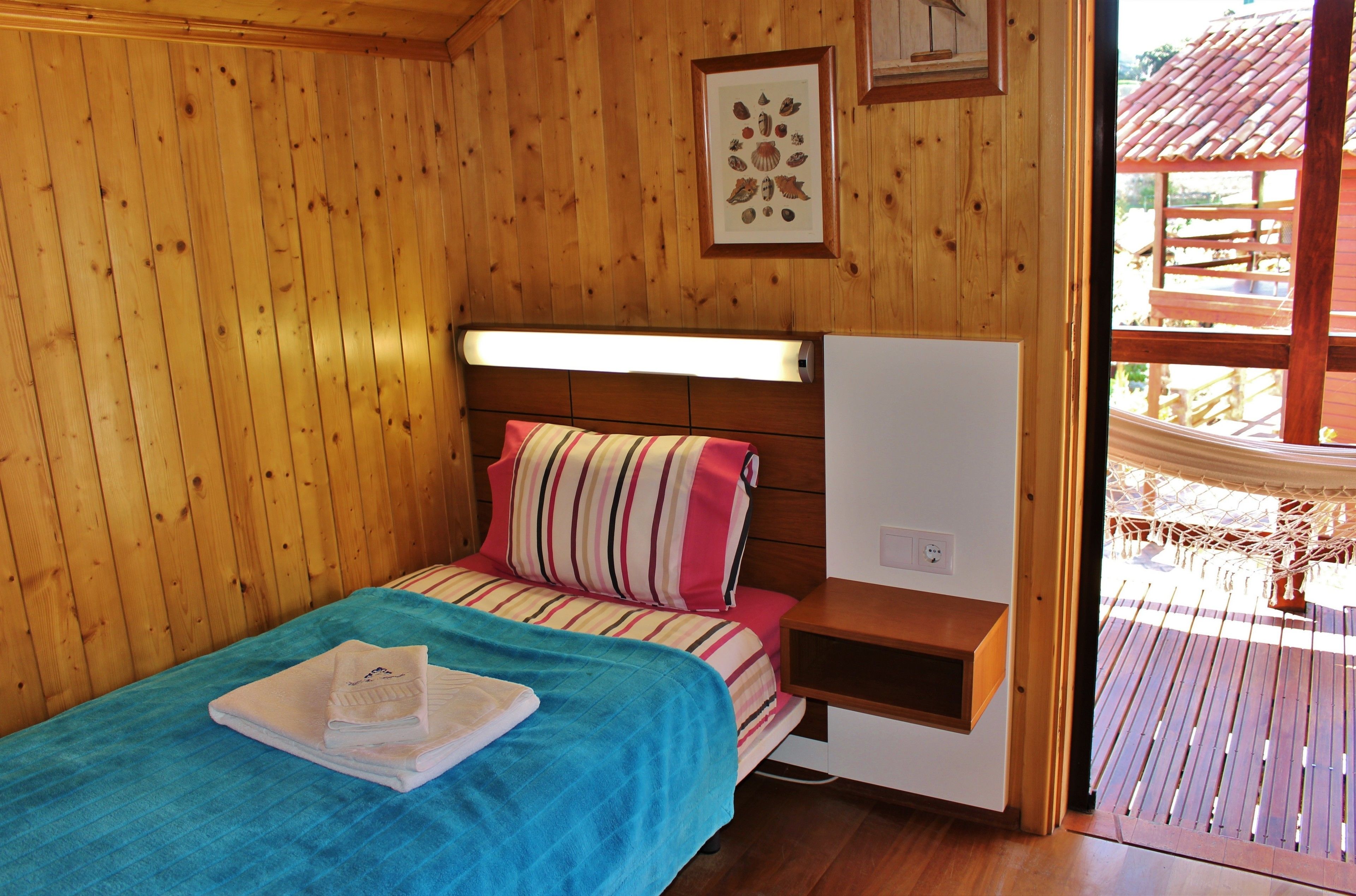 Una habitación de cabaña de madera con una cama, una mesita de noche pequeña y un cuadro en la pared.