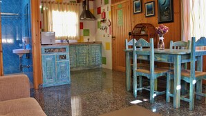 Un intérieur en bois comprenant un coin cuisine, une table à manger, des chaises et un buffet bleu.