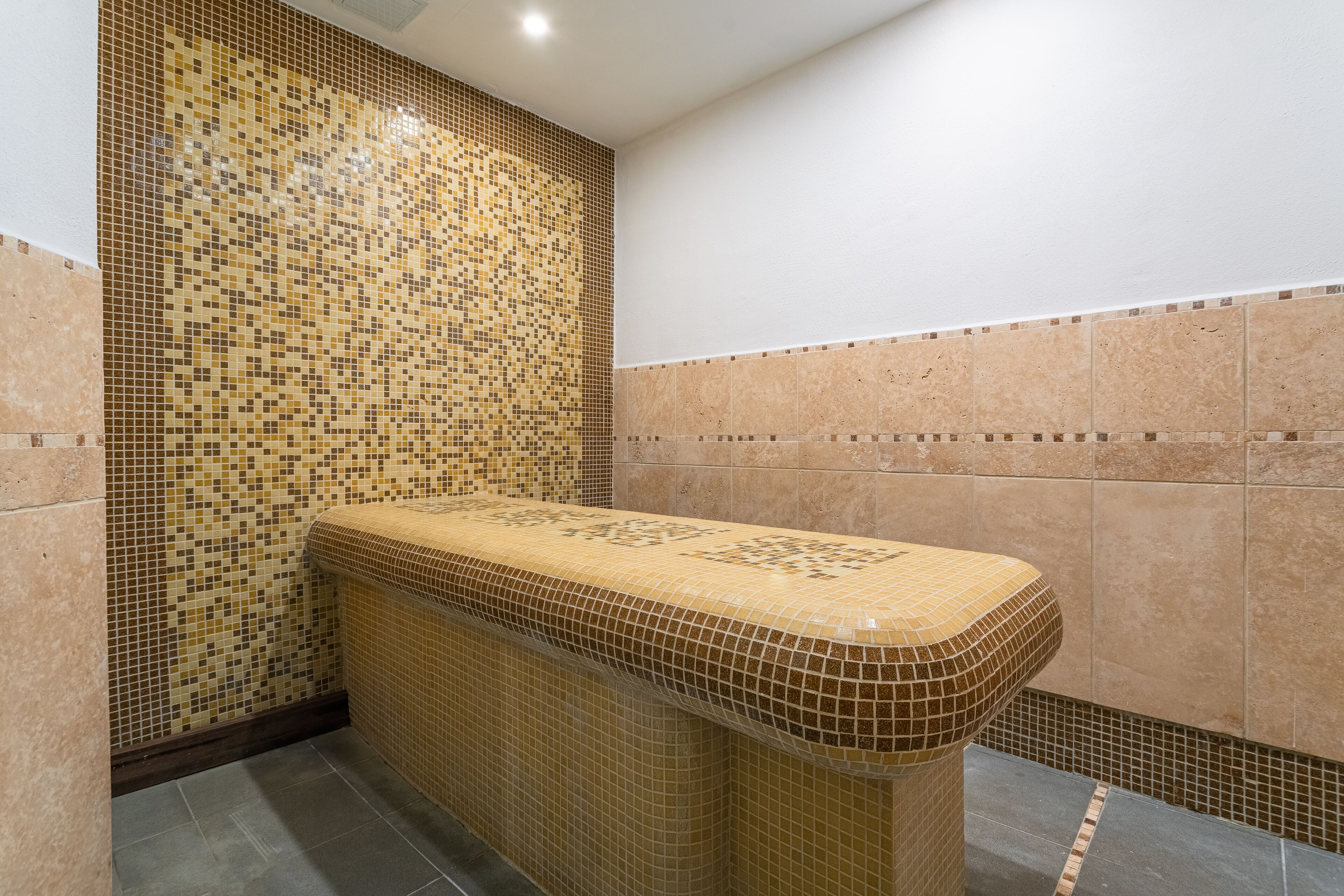 Une salle de bain avec des murs recouverts de mosaïques, un banc carrelé et un sol carrelé.