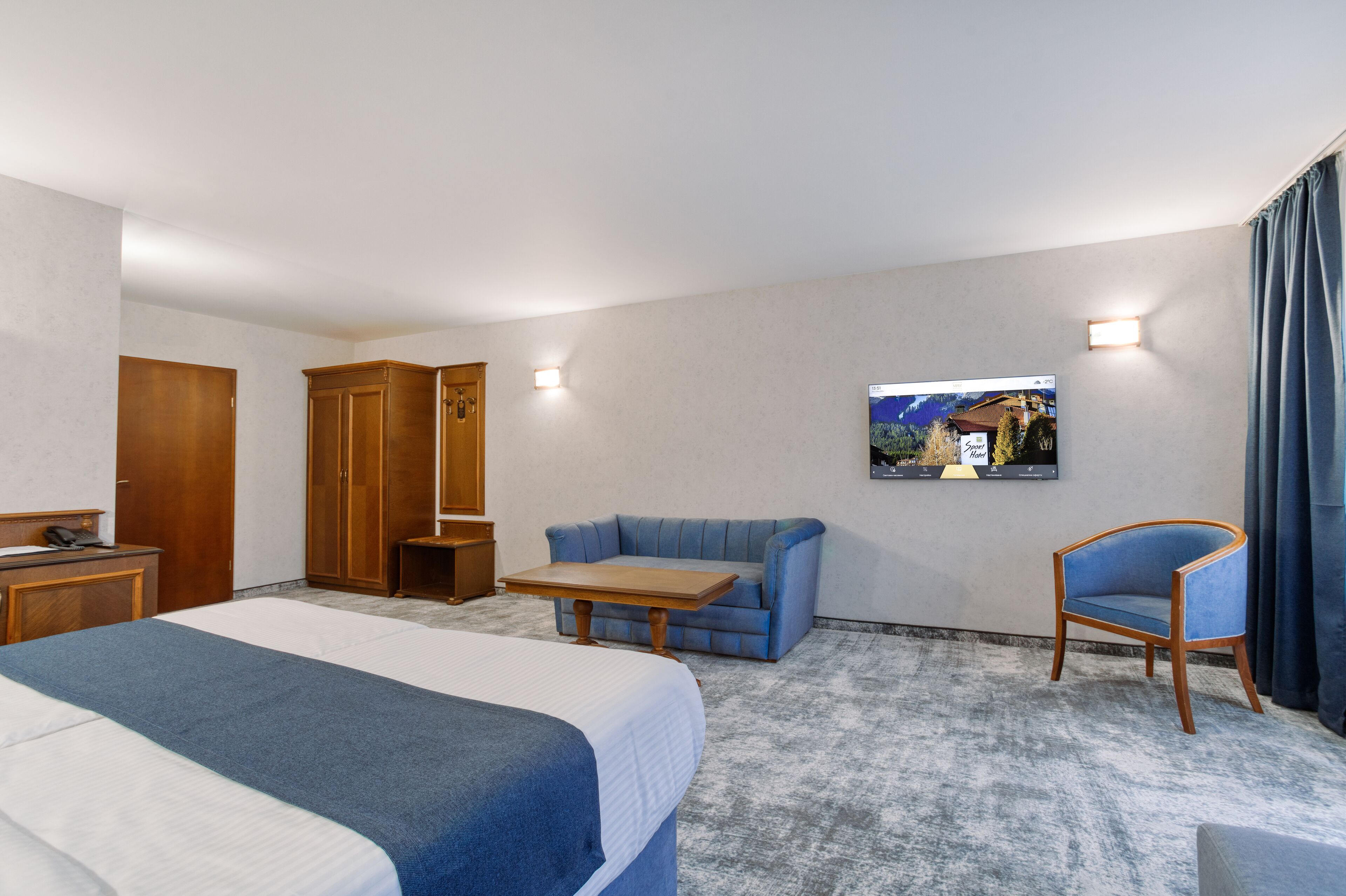 A hotel room with a bed, a desk, a wardrobe, a seating area with a table, and a TV mounted on the wall.