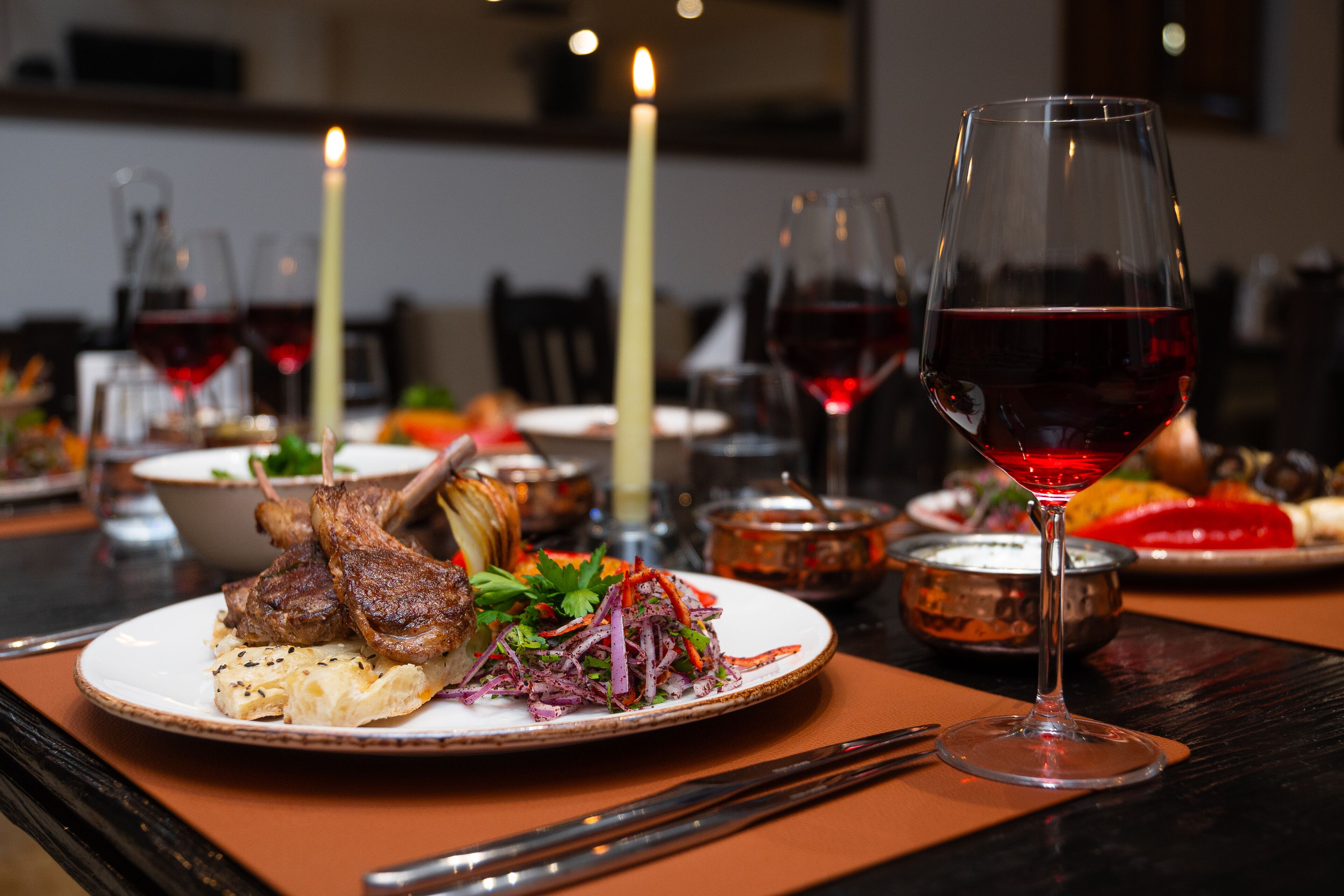 A dining table set with plates of food, glasses of red wine, and candles.