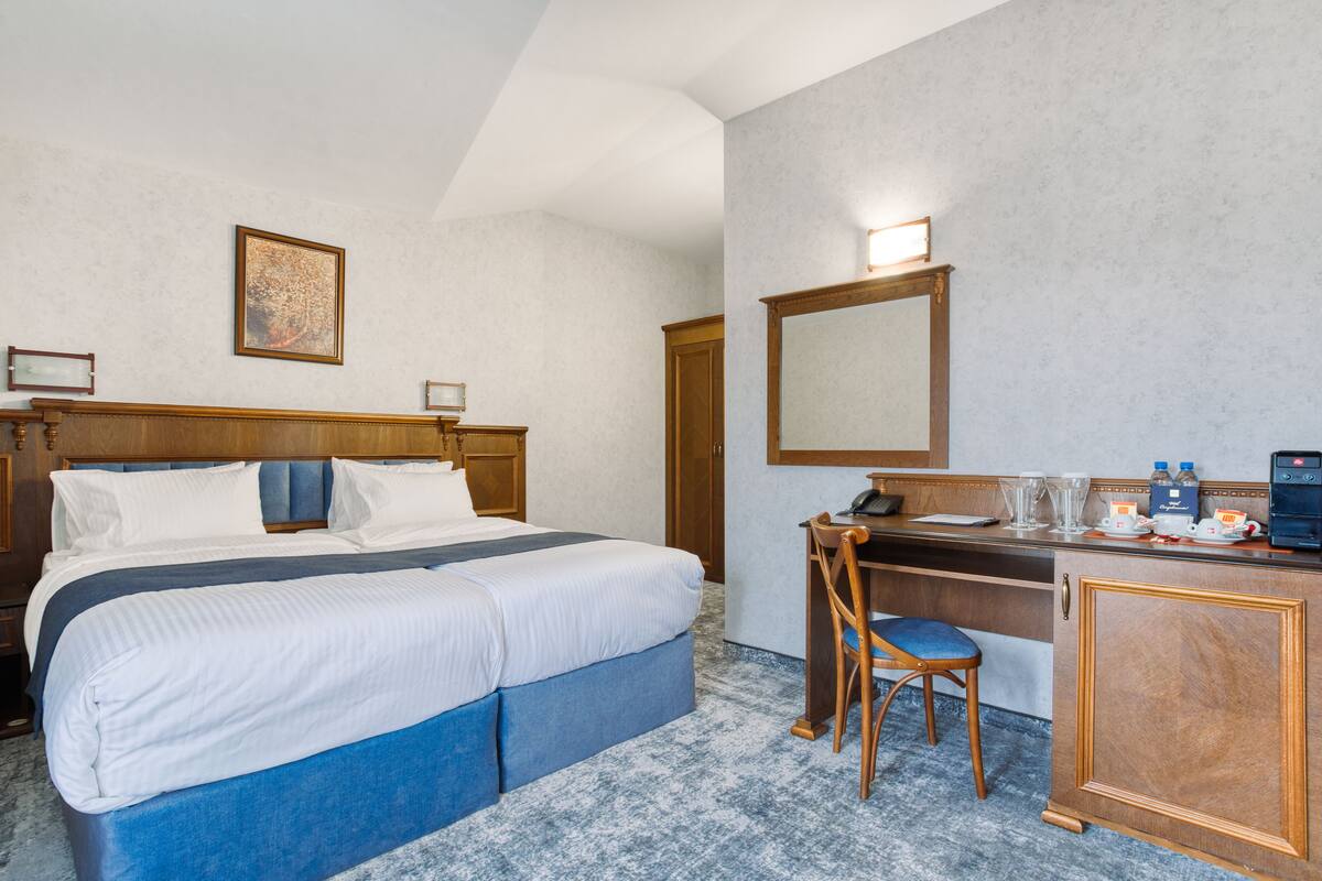 A hotel room with a bed, a desk, a chair, a mirror, and a coffee maker.