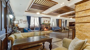 A spacious living room with a fireplace, wooden ceiling beams, and comfortable seating. - MPM Sport Hotel (Bansko)