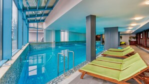 An indoor swimming pool with clear glass walls, a tiled floor, and lounge chairs along the poolside. - MPM Sport Hotel (Bansko)