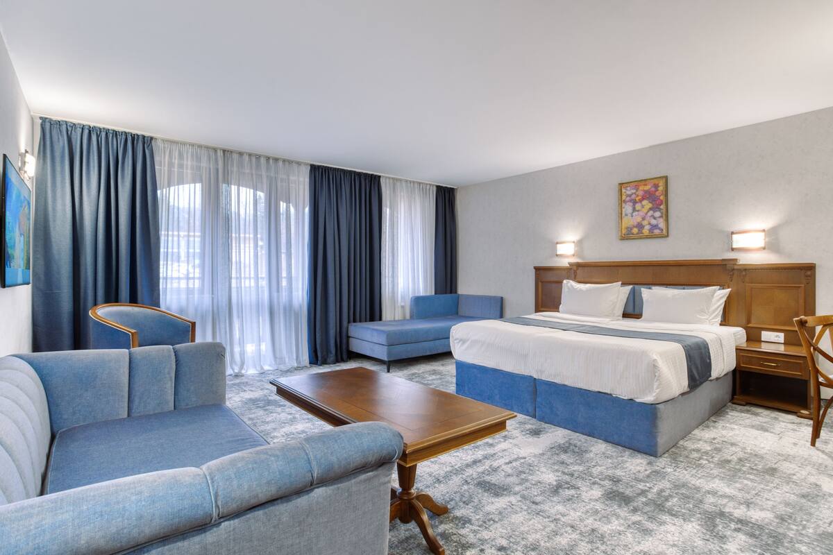 A hotel room with a bed, two sofas, a wooden coffee table, and a nightstand.