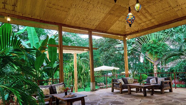 Un espacio de estar al aire libre cubierto con suelo de piedra, mobiliario de madera y exuberante vegetación tropical.