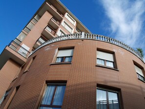 Un immeuble à plusieurs étages doté d’une façade incurvée, avec des balcons pourvus de rampes en métal et des fenêtres avec des volets blancs.