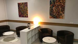 A modern lounge area with a white reception desk, leather armchairs, a round white table, and abstract paintings on the walls. - Pensión La Salve (Bilbao)