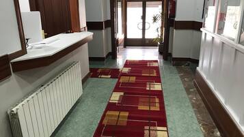 A hotel hallway with a patterned carpet, a reception desk, and a radiator.