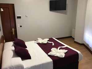 A hotel room with a bed, a TV mounted on the wall, and a door. - Pensión La Salve (Bilbao)