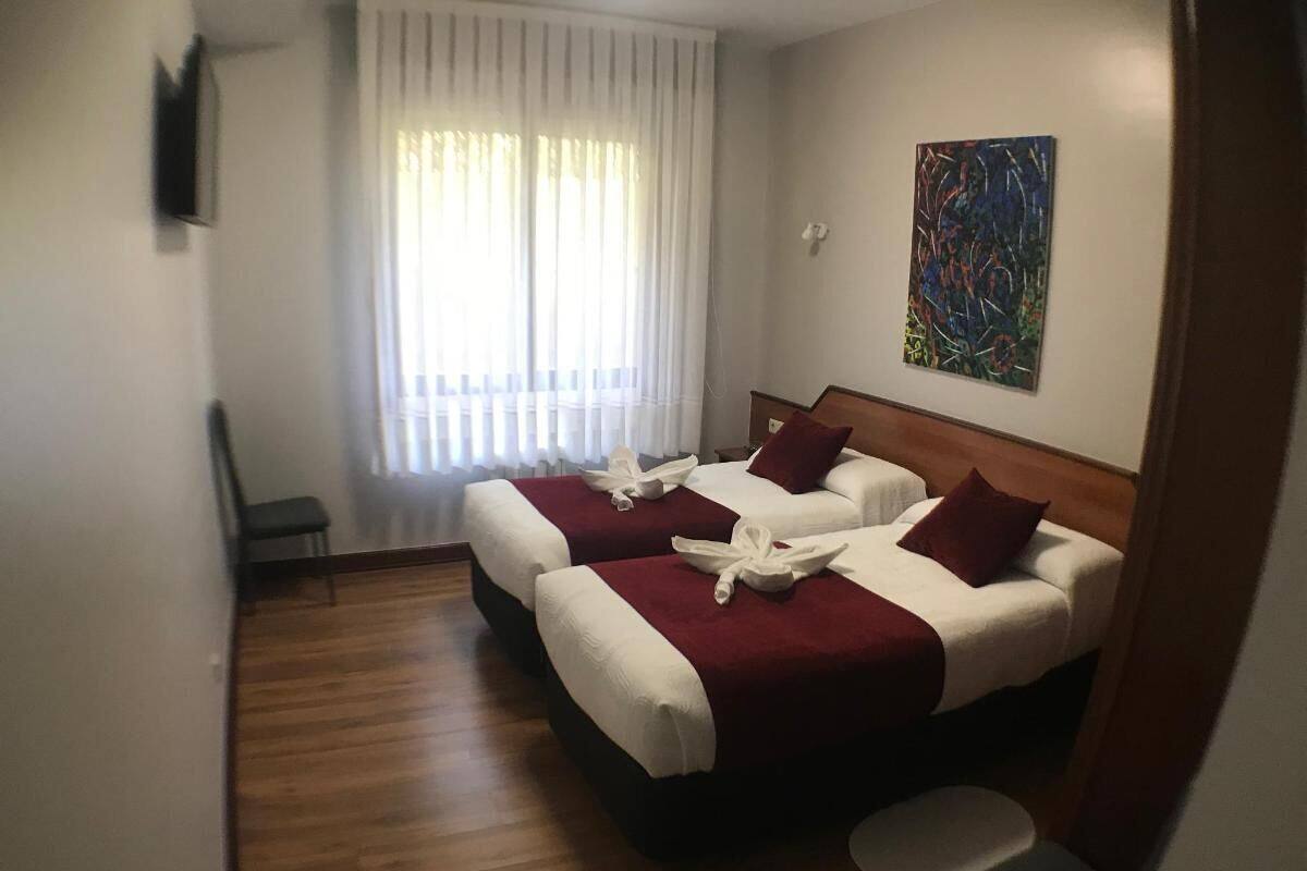 Une chambre d’hôtel avec deux lits, un plancher en bois, une fenêtre avec des rideaux et un tableau au mur.