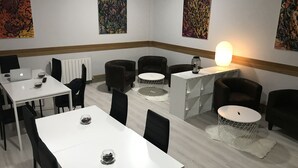 A modern, well-lit room with white tables and black chairs, featuring abstract art on the walls and a central white table with a lamp. - Pensión La Salve (Bilbao)