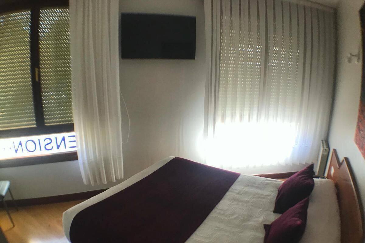 Une chambre à coucher avec un lit, un téléviseur fixé au mur et une fenêtre avec des rideaux.