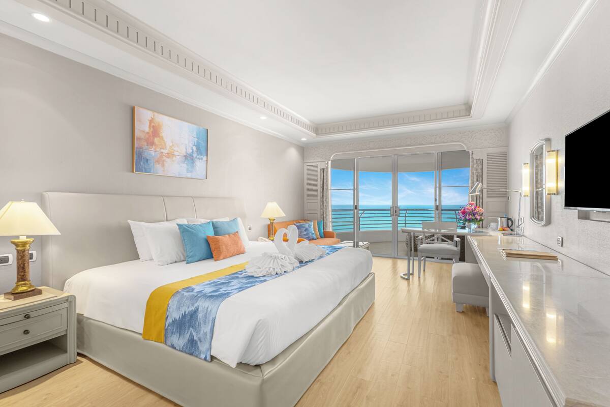 A hotel room with a large bed, a desk, a view of the ocean, and a television.