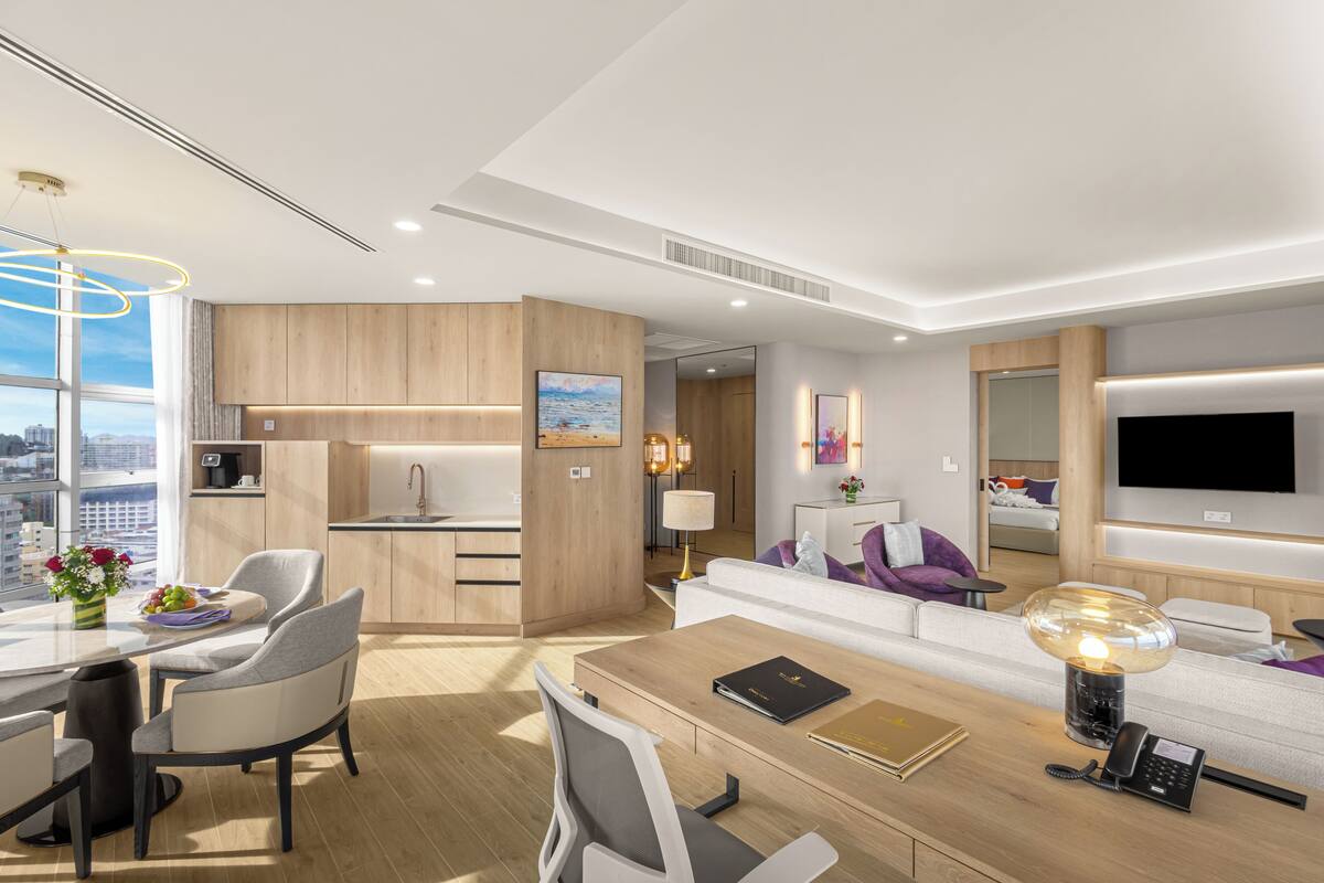 A modern hotel room with a dining area, a sofa, a TV, and a city view.