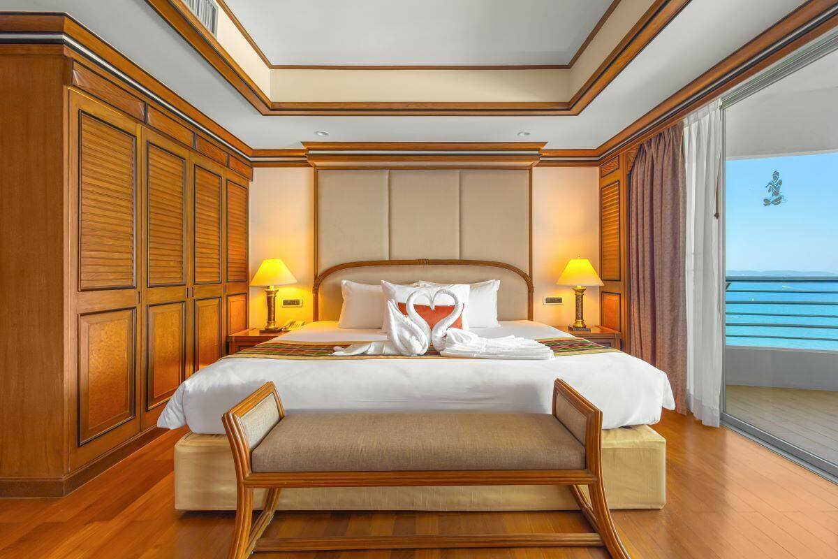 A spacious hotel room with a large bed, wooden paneling, two bedside lamps, and a view of the ocean.