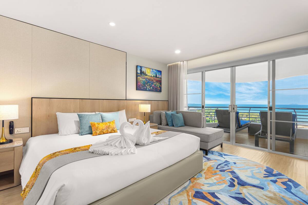 A hotel room with a large bed, a sofa, a balcony with chairs, and a painting on the wall.