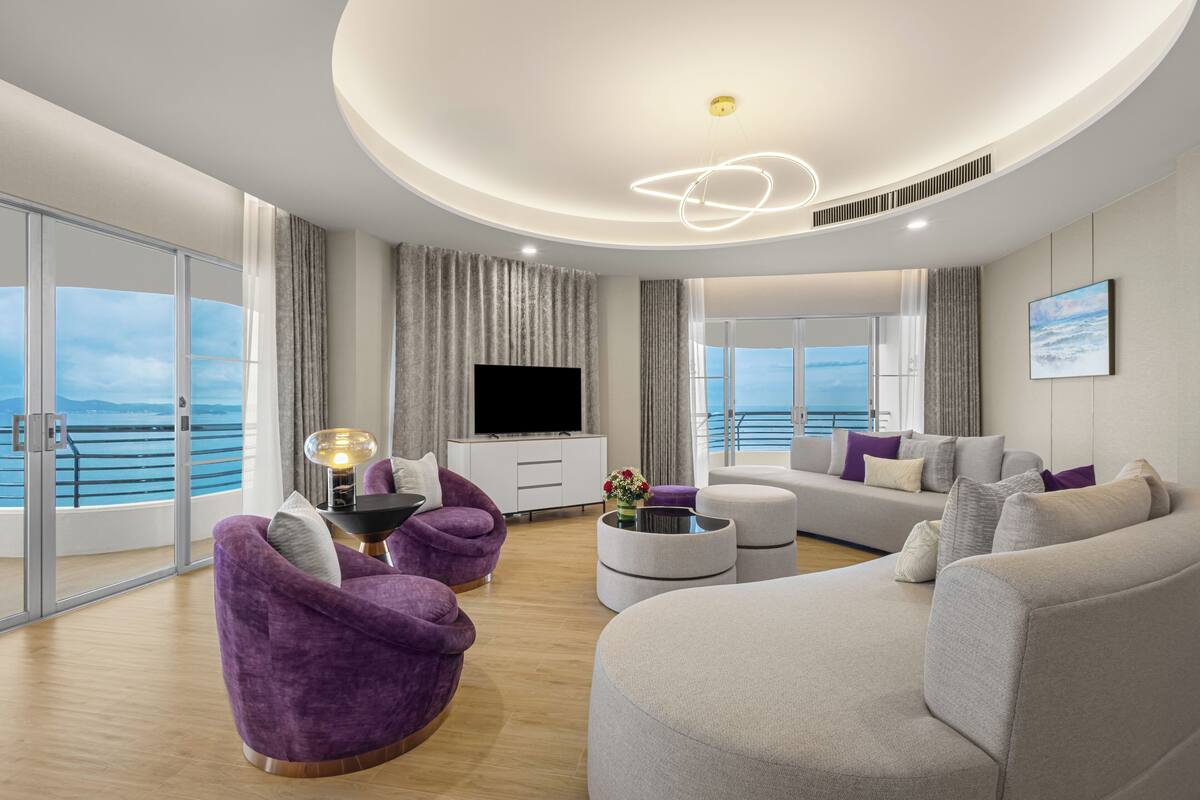 A modern living room with a large TV, comfortable seating, and a view of the sea.