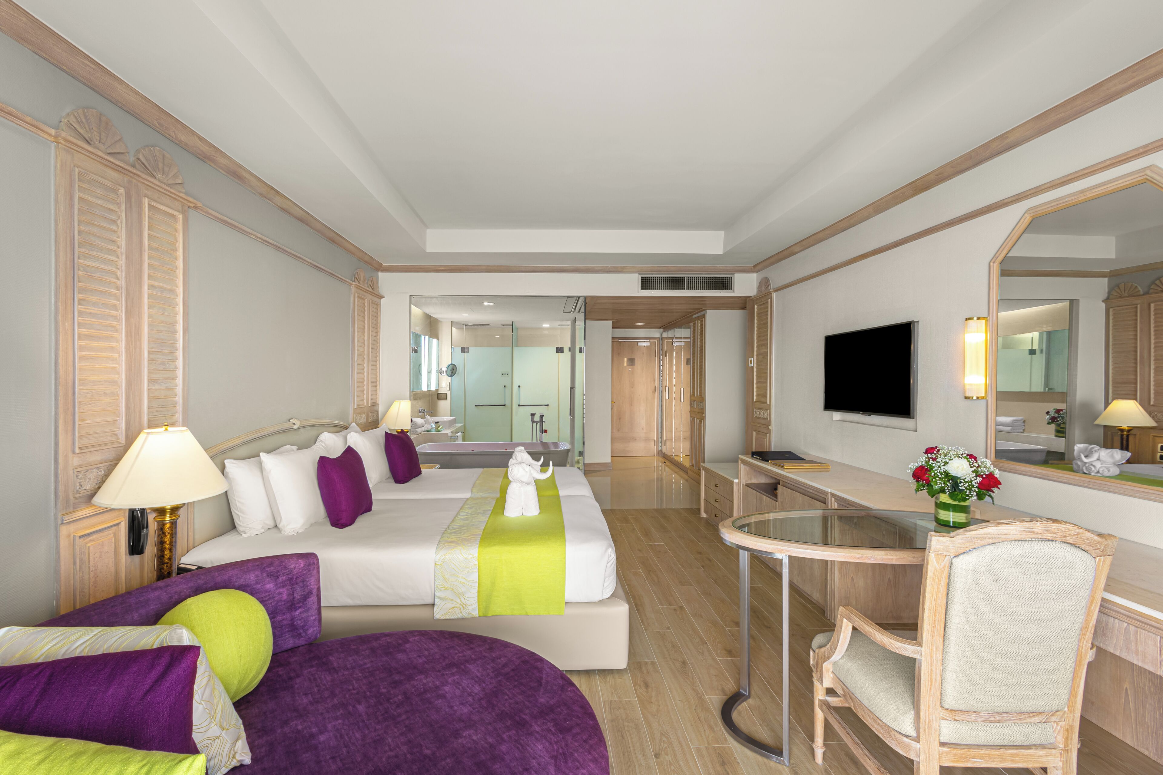 A hotel room with a bed, a desk, a chair, a TV, and a bathroom visible in the background.