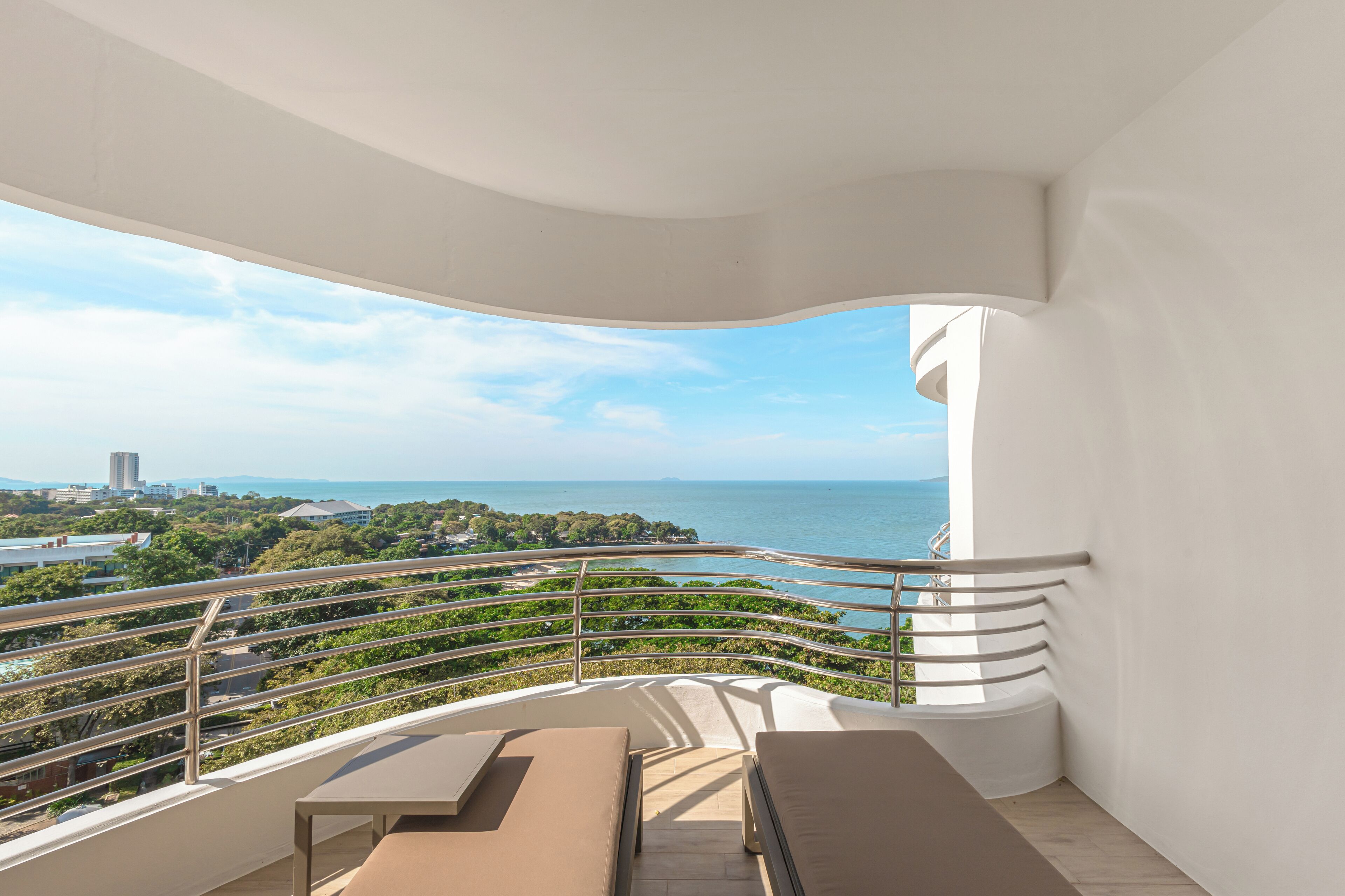 A balcony with a view of the sea, a white railing, and a bench.