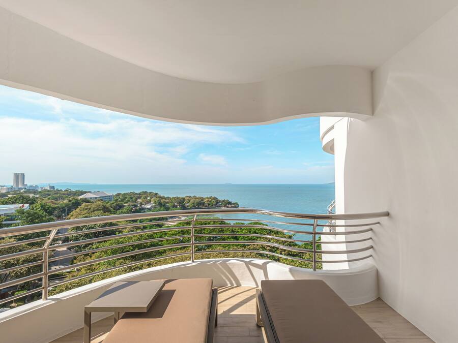 A balcony with a view of the sea, a white railing, and a bench.