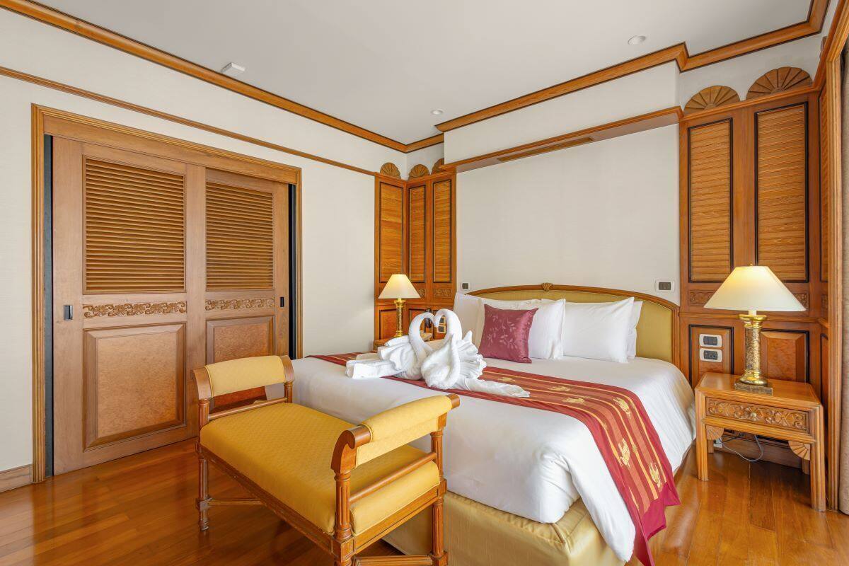 A hotel room with two beds, wooden paneling, a bench, and a nightstand with lamps.
