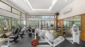 Une salle de sport moderne équipée de machines de cardio, d’appareils de musculation et de grandes fenêtres donnant sur un paysage arboré.