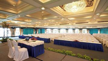 A large conference room with rows of white chairs, a stage with a blue tablecloth, and a chandelier.