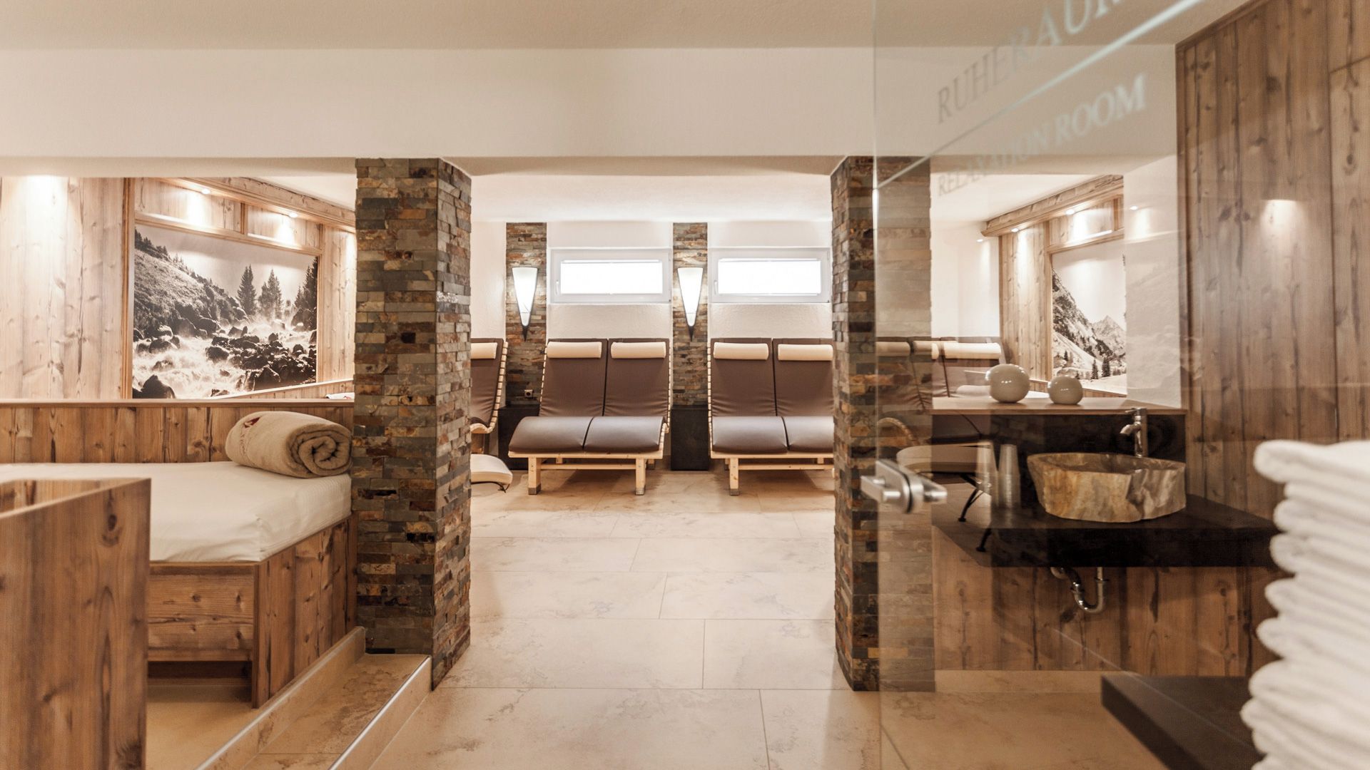 Ein Spa-Raum mit Steinwand, einer Holzbank, einem Massagetisch und einem Waschbecken.