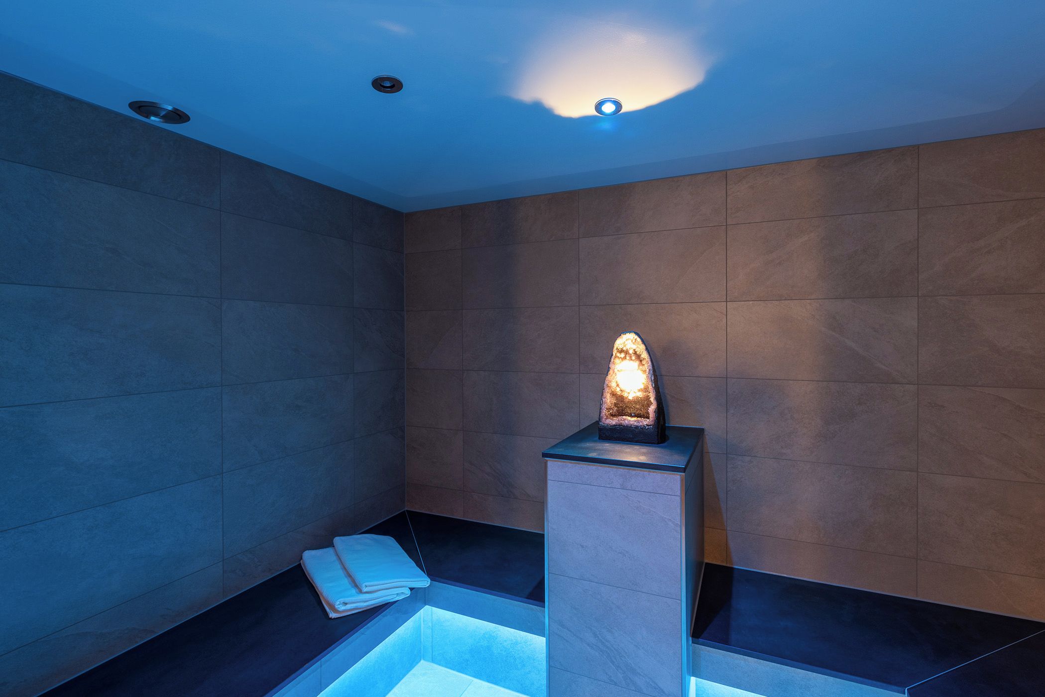 A modern bathroom with a central heated stone feature, a small sink, and a towel rack.