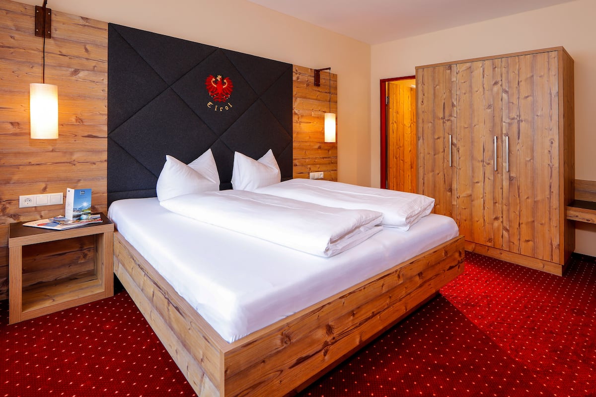 Ein Doppelbett mit Holz-Kopfstück, ein Kleiderschrank und ein roter Teppichboden.