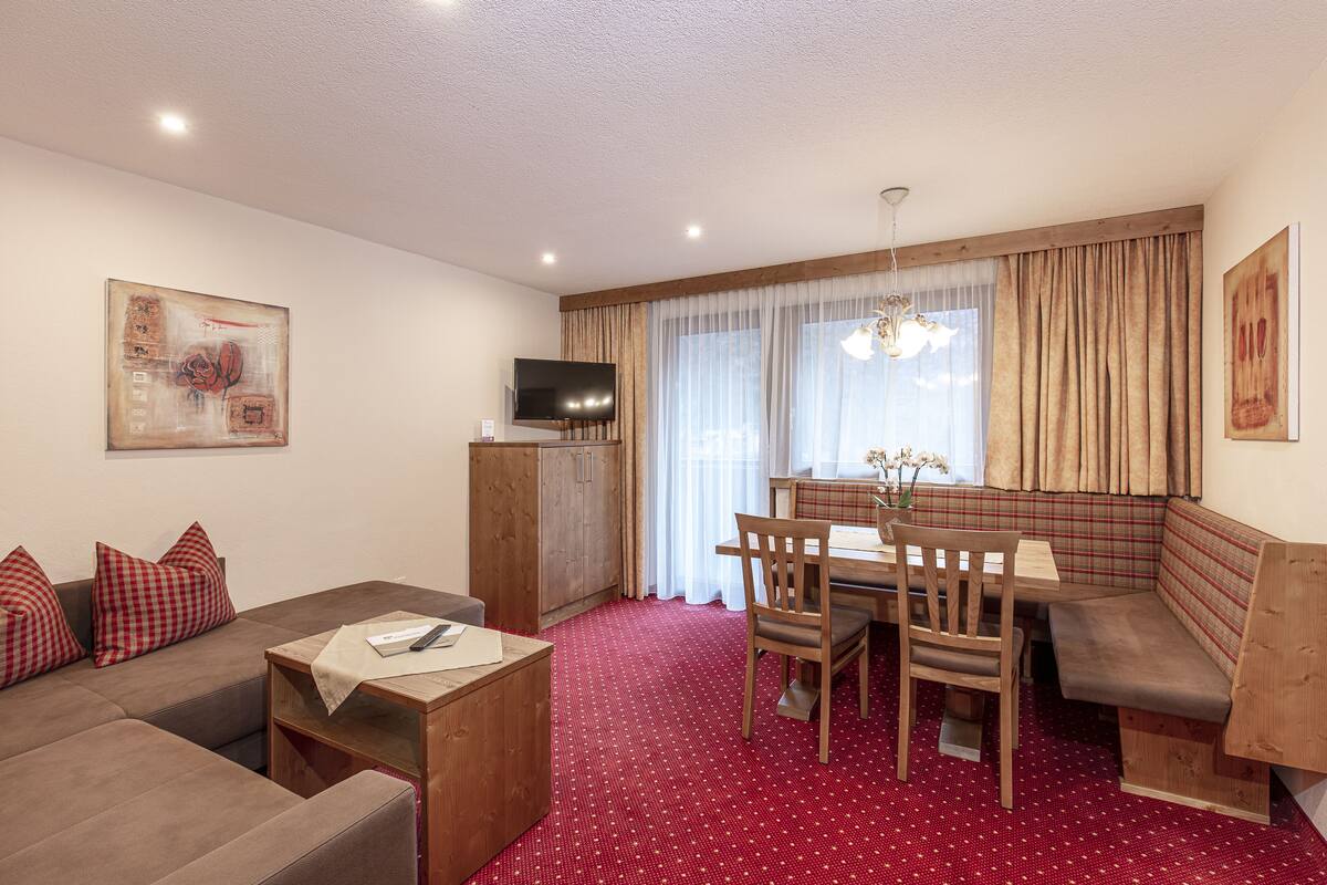 Ein modernes Wohnzimmer mit einer Couch, einem Esstisch mit Stühlen, einem Fernseher und einem roten Teppich mit Muster.